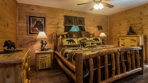 A log cabin-style bedroom with a wooden bed, two bedside tables, a ceiling fan, and a bear-themed decor.