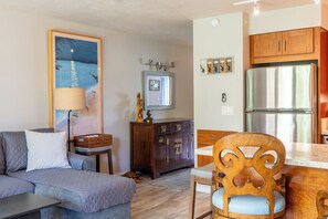 Una sala de estar con un sofá, un aparador de madera, una mesa de comedor con sillas y una cocina con refrigerador.