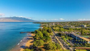 Paesaggio costiero con spiaggia, edifici e montagne sullo sfondo.