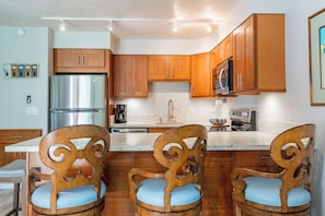 A modern kitchen with wooden cabinets, stainless steel appliances, and a central island with chairs.
