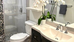 Une salle de bain moderne avec une douche à parois de verre, des toilettes, un meuble-lavabo avec un miroir et des orchidées blanches.