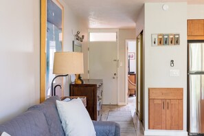A living room with a sofa, a lamp, a wooden cabinet, and a kitchen area with a refrigerator and cabinets.