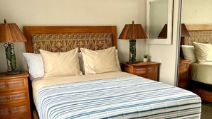 Une chambre à coucher avec un lit en bois, deux tables de chevet avec des lampes, une tête de lit ornée d’un motif et un grand miroir au mur.