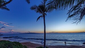 A beach scene with palm trees, a clear sky, and a calm sea. - Tropical Centrally Located Condo Steps from Kamaole II Beach (Kihei)
