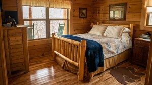 A wooden cabin bedroom with a bed, a desk, and a window with a view of trees. - Honeymoon/couples Retreat -  Private Custom Built Log Cabin - Wi-fi (Sevierville)