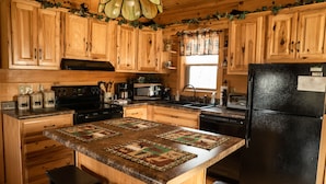 A kitchen with wooden cabinets, a black refrigerator, and a central island with a quilted runner. - Honeymoon/couples Retreat -  Private Custom Built Log Cabin - Wi-fi (Sevierville)