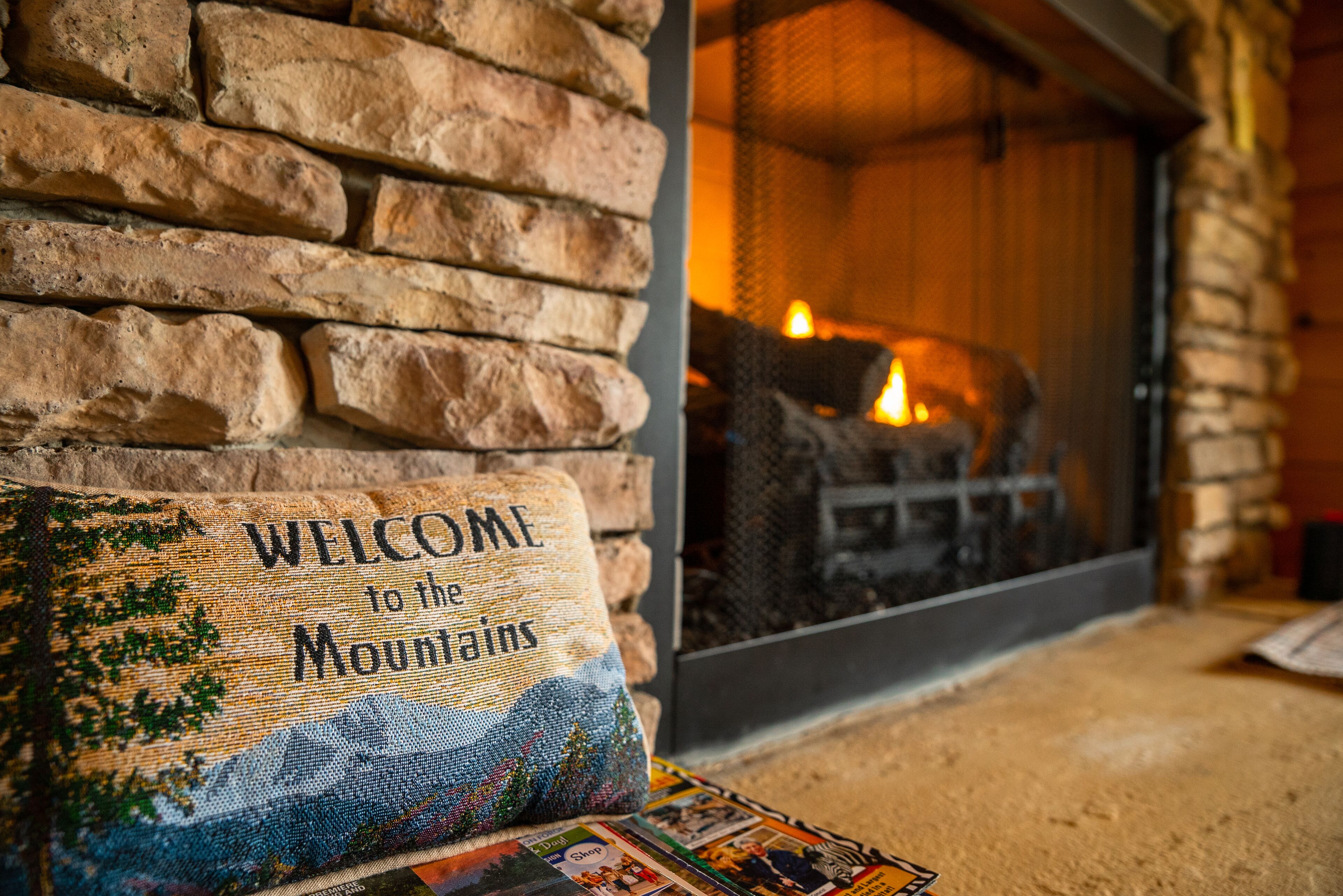 A stone wall with a 'Welcome to the Mountains' sign and a fireplace with a fire.
