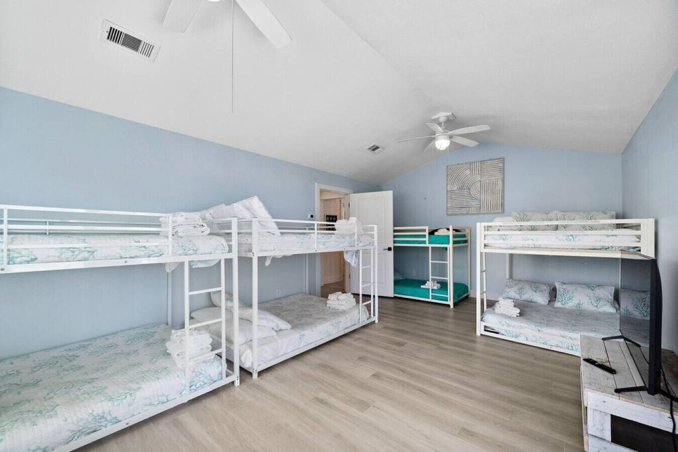 Ein Zimmer mit Etagenbetten, einem Deckenventilator und einer Tür zu einem weiteren Raum.