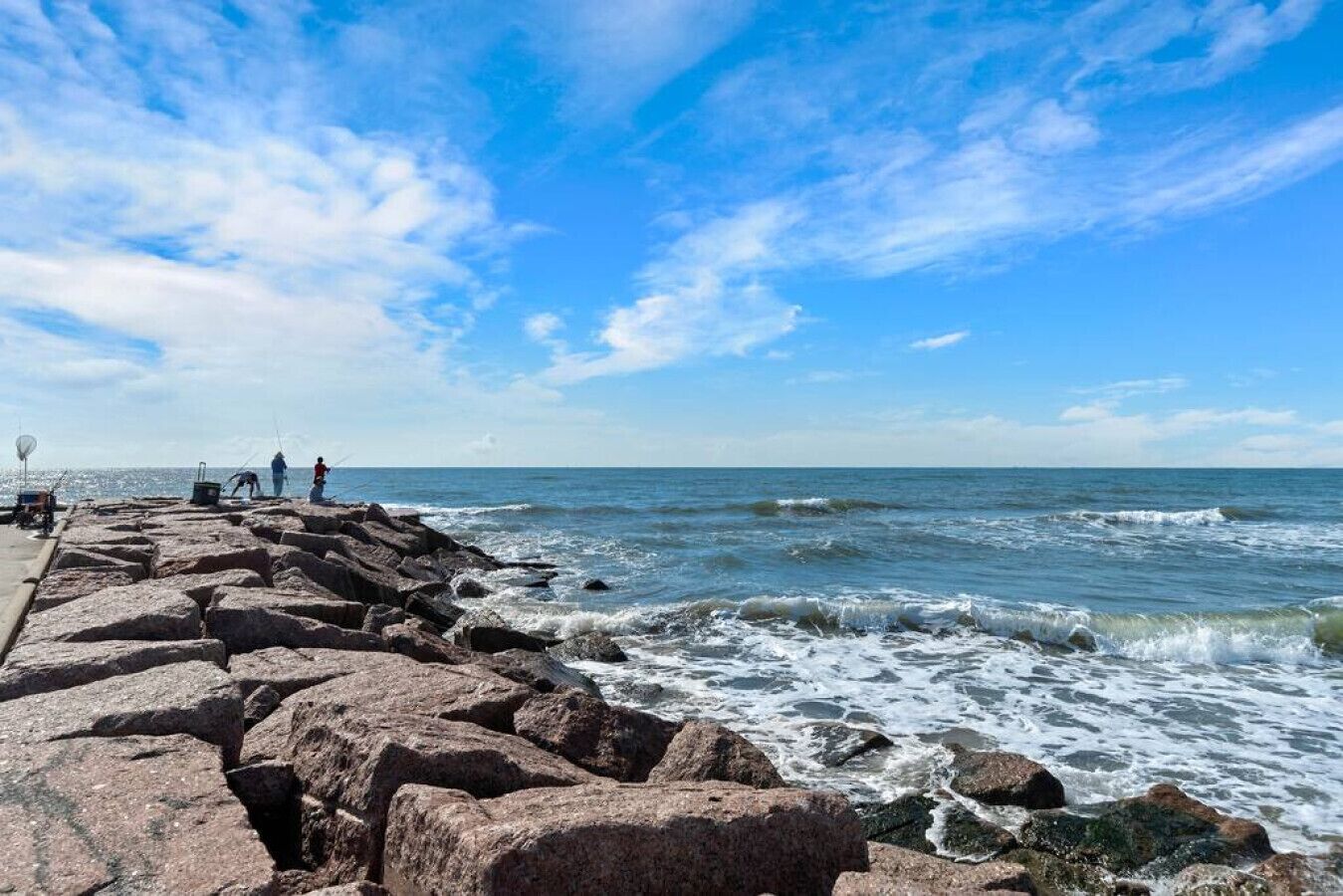 En stenet mole med bølger der slår mod den, under en klar blå himmel.