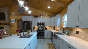 Une cuisine moderne avec des armoires blanches, un grand îlot central, des appareils en acier inoxydable et un plafond en bois.
