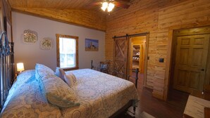 Une chambre avec un plafond en bois, un lit avec une literie à motifs, une fenêtre et une porte donnant sur un placard.