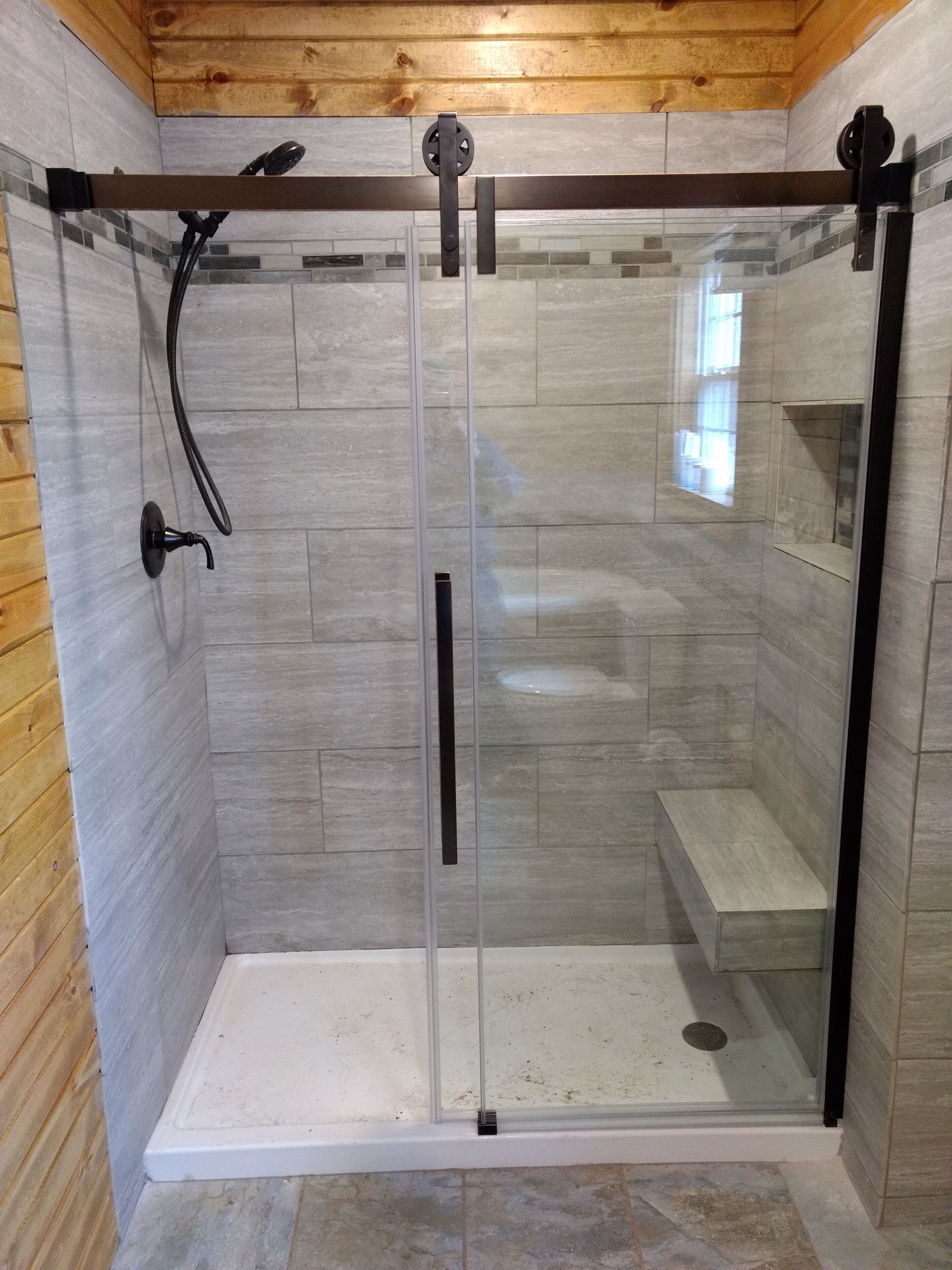 A glass-enclosed shower with a bench, wooden walls, and a tiled floor.