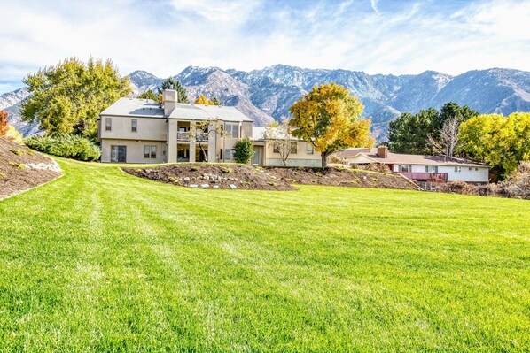 A large, two-story house with a well-maintained lawn and a mountain backdrop.