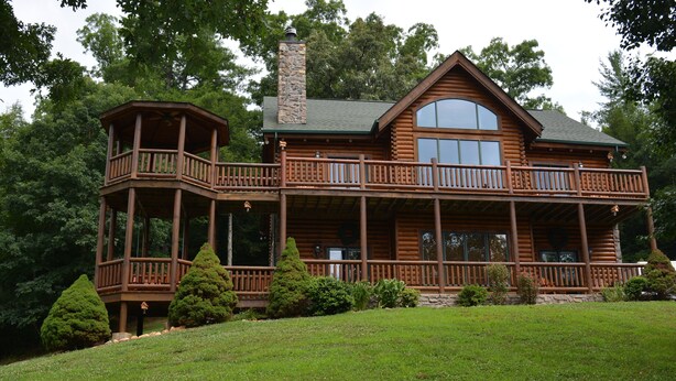 A log cabin with a two-story balcony, a stone chimney, and a large window. - SPACIOUS FAMILY RETREAT NEAR ALL THE FUN! STUNNING VIEW, EASY ACCESS. (Sevierville)