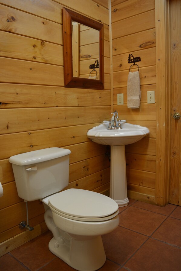 Une salle de bain aux murs lambrissés, avec des toilettes blanches, un lavabo et un miroir.