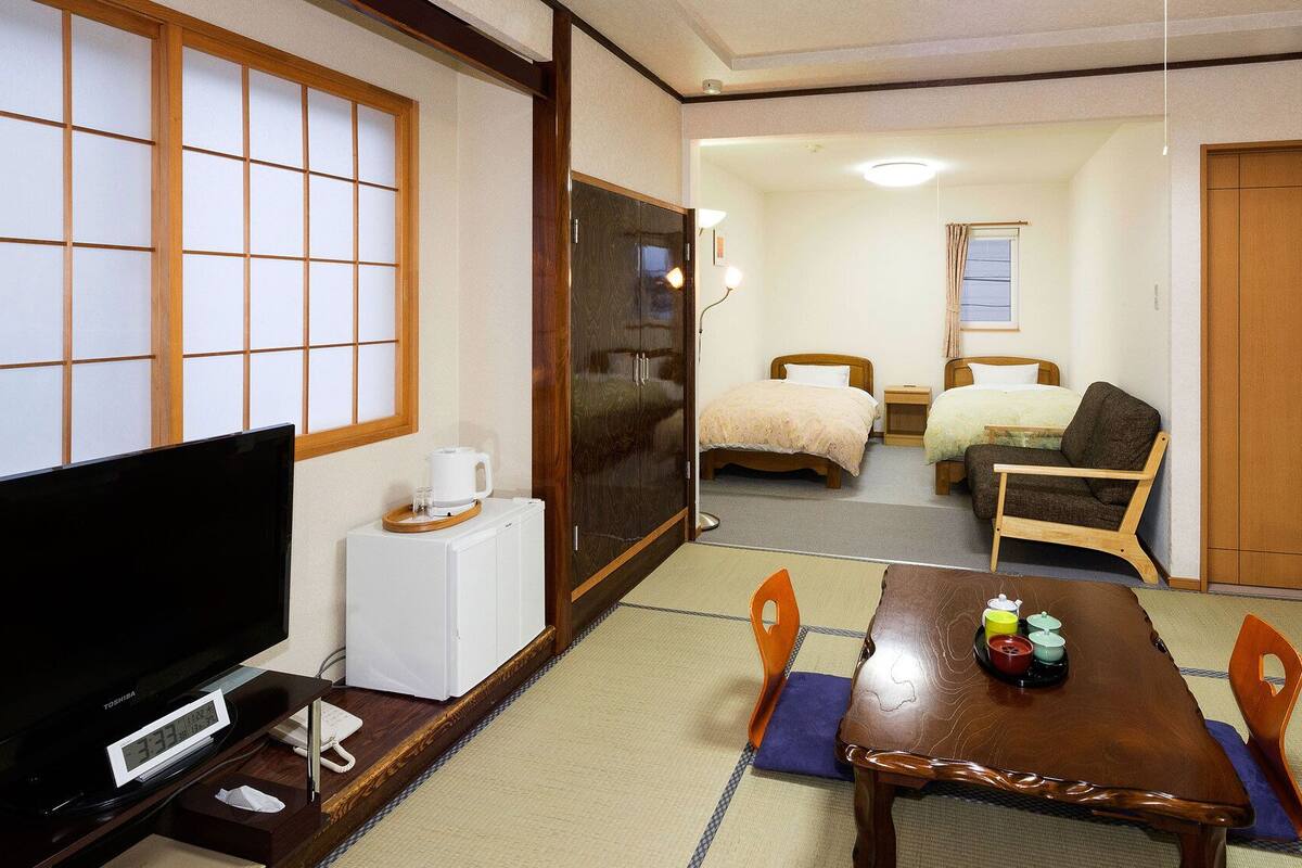 Ein traditioneller japanischer Raum mit Tatami-Boden, einem Fernseher, einem Holztisch mit Teeservice und zwei Betten.