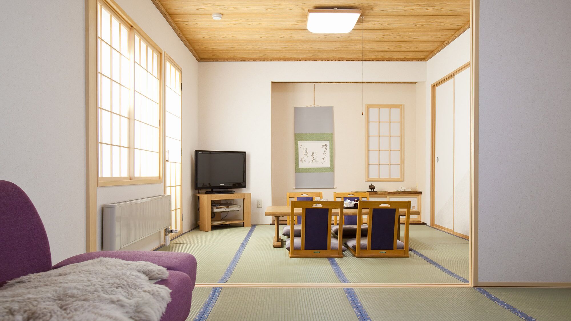 Perinteinen japanilainen huone, jossa on tatamimatto lattiana, televisio, tatamimatosta tehty pöytä ja violetti sohva.