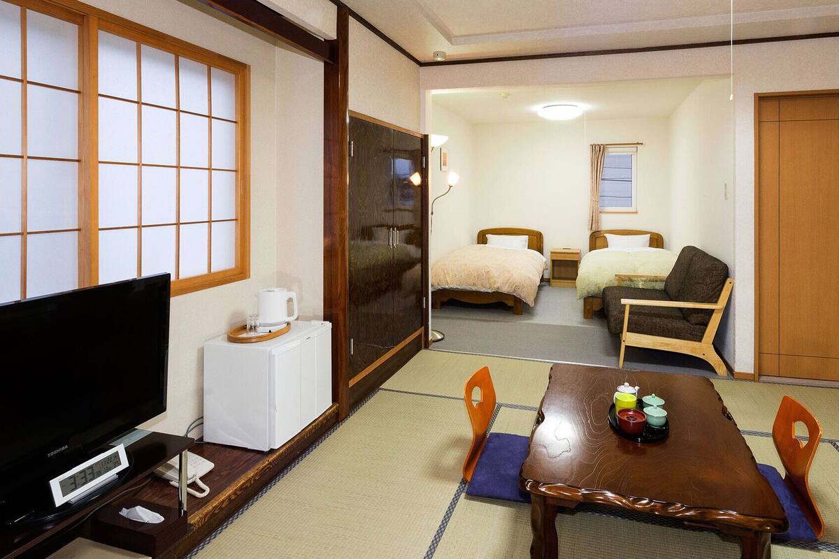Ein traditioneller japanischer Raum mit Tatami-Böden, einem Fernseher, einem Holztisch mit Teeservice und zwei Betten.