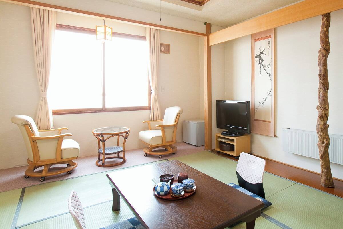 Ein traditioneller japanischer Raum mit Tatami-Boden, einem Fernseher und einem Esstisch, gedeckt mit Teekannen und Tassen.