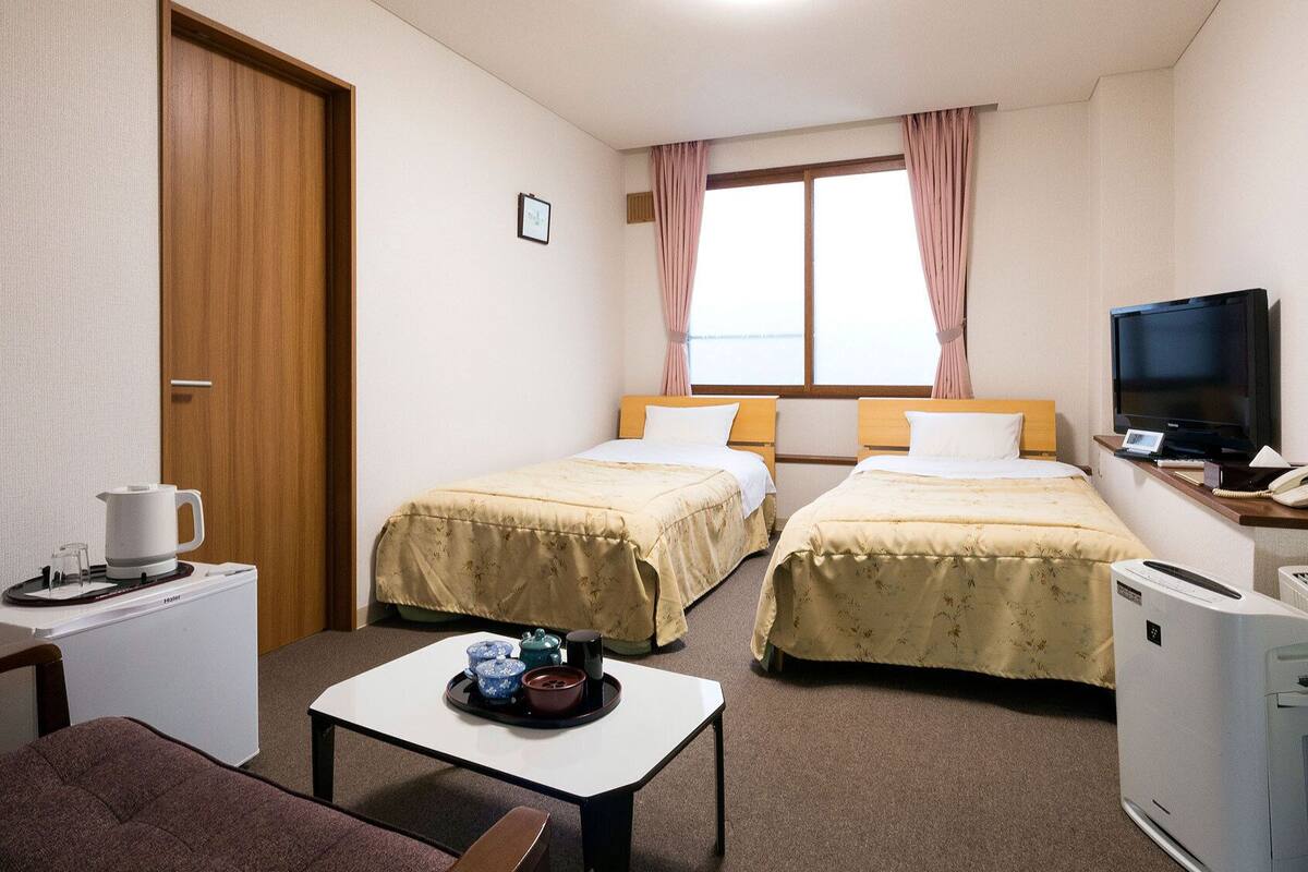 Ein Hotelzimmer mit zwei Betten, einem Fernseher, einem Schreibtisch mit Wasserkocher und einer Heizung.