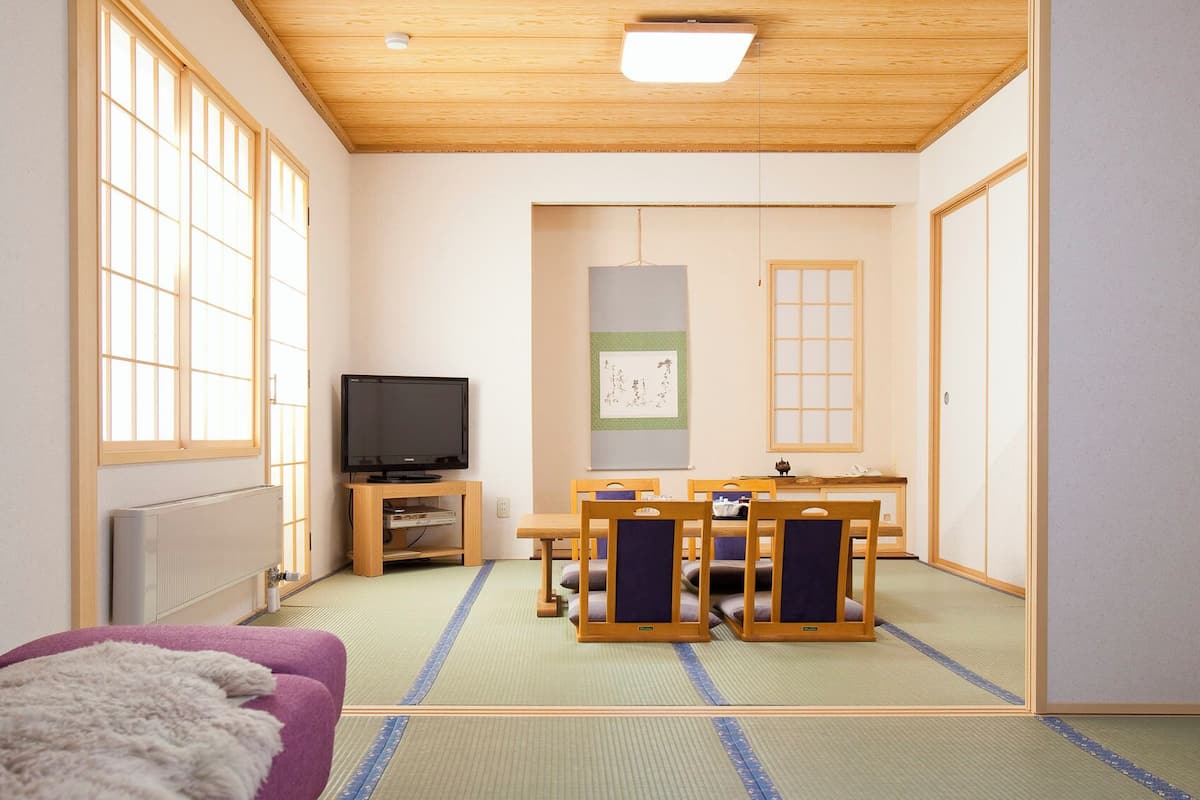 Ett traditionellt japanskt rum med tatamimattor på golvet, en tv, ett bord med stolar som också är tillverkat av tatamimattor, och en shoji-skärm.