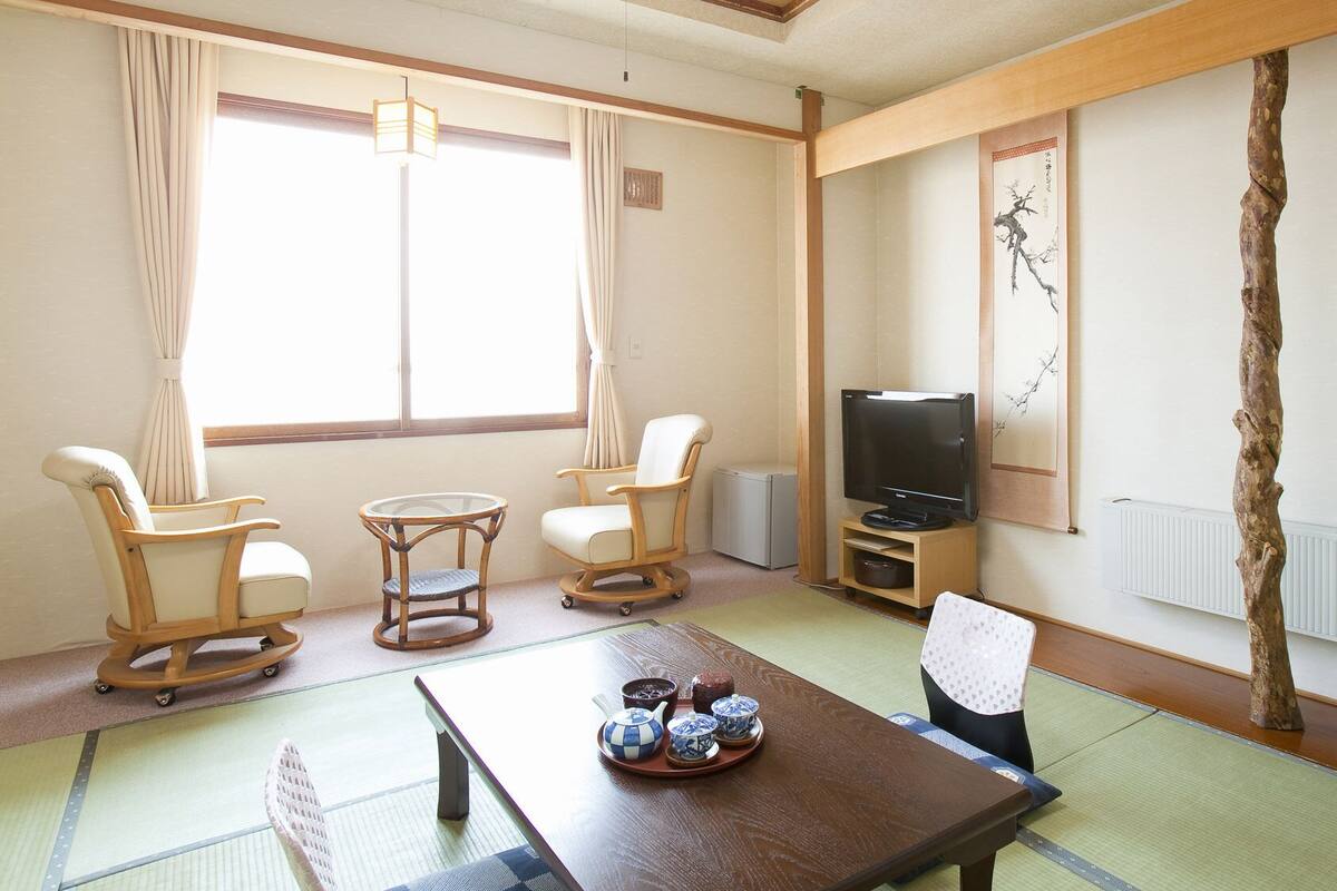 Ein traditioneller japanischer Raum mit Tatami-Böden, einem Fernseher und einer Holzstamm-Dekoration.