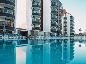 A modern hotel with a swimming pool, multiple balconies, and lounge chairs. - grand uysal (alanya tosmur)