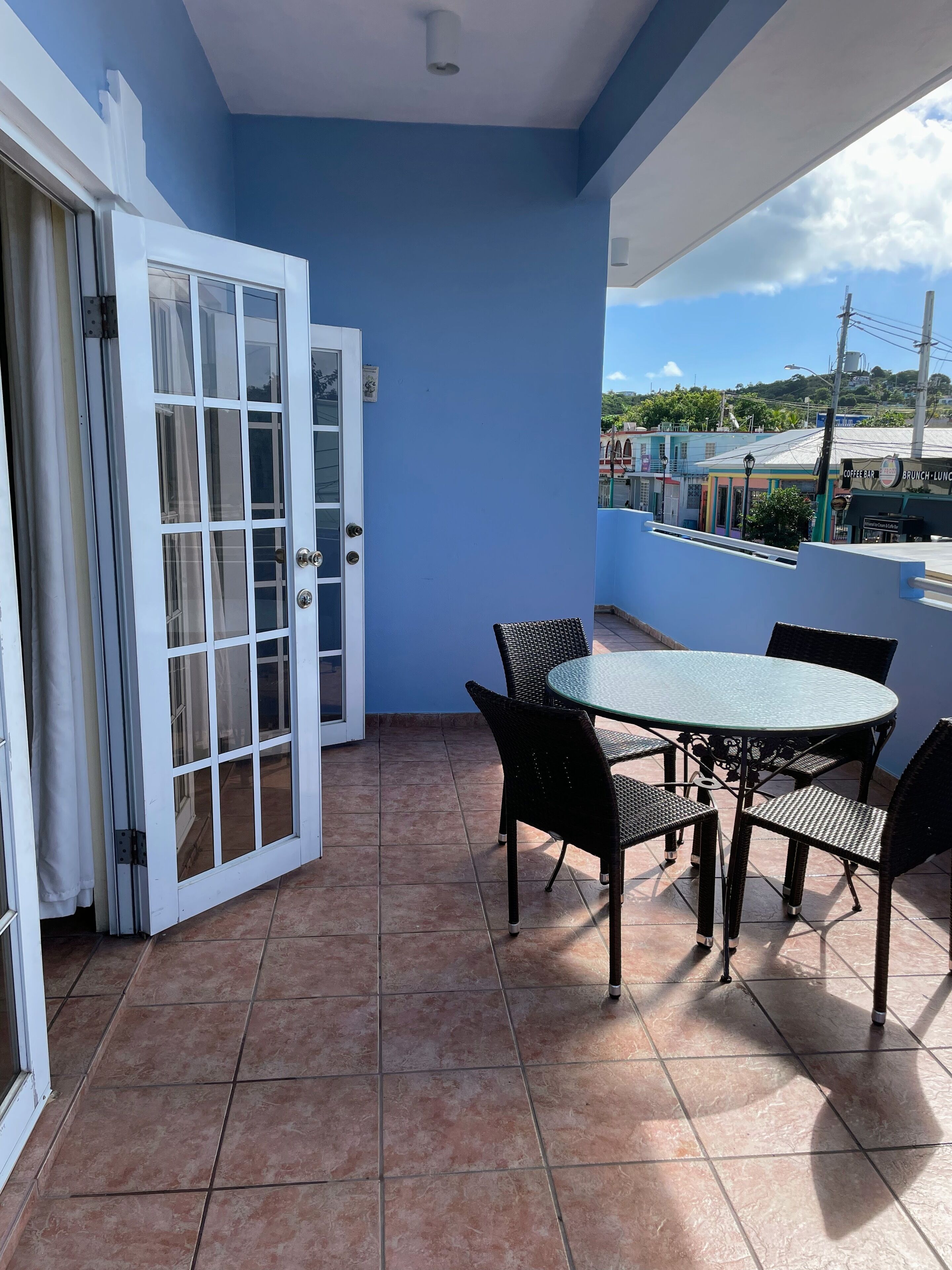 A balcony with a blue wall, a glass door, and a round table with chairs.