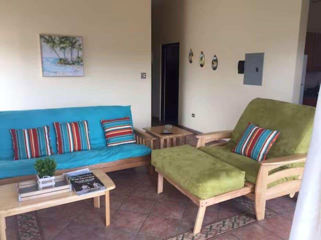 A living area with a blue sofa, a green armchair, and a small table with a plant and books.