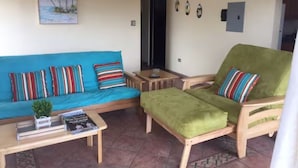 Ein Wohnbereich mit blauem Sofa, grünem Sessel und einem kleinen Tisch mit Pflanze und Büchern.