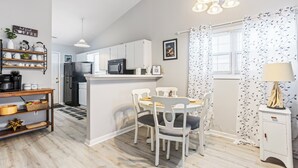 A modern kitchen with white cabinets, a black refrigerator, and a microwave. There is a dining area with a white table and chairs.