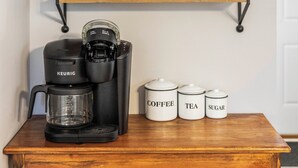A coffee station with a Keurig machine, white mugs, and labeled containers for coffee, tea, and sugar.