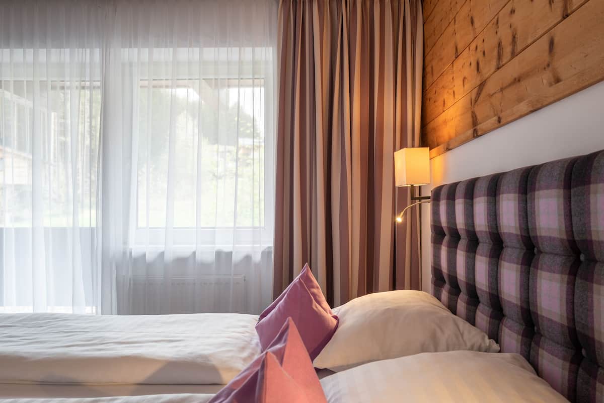 Una habitación de hotel con cama, cortinas, una lámpara de pared y cabecera de madera.