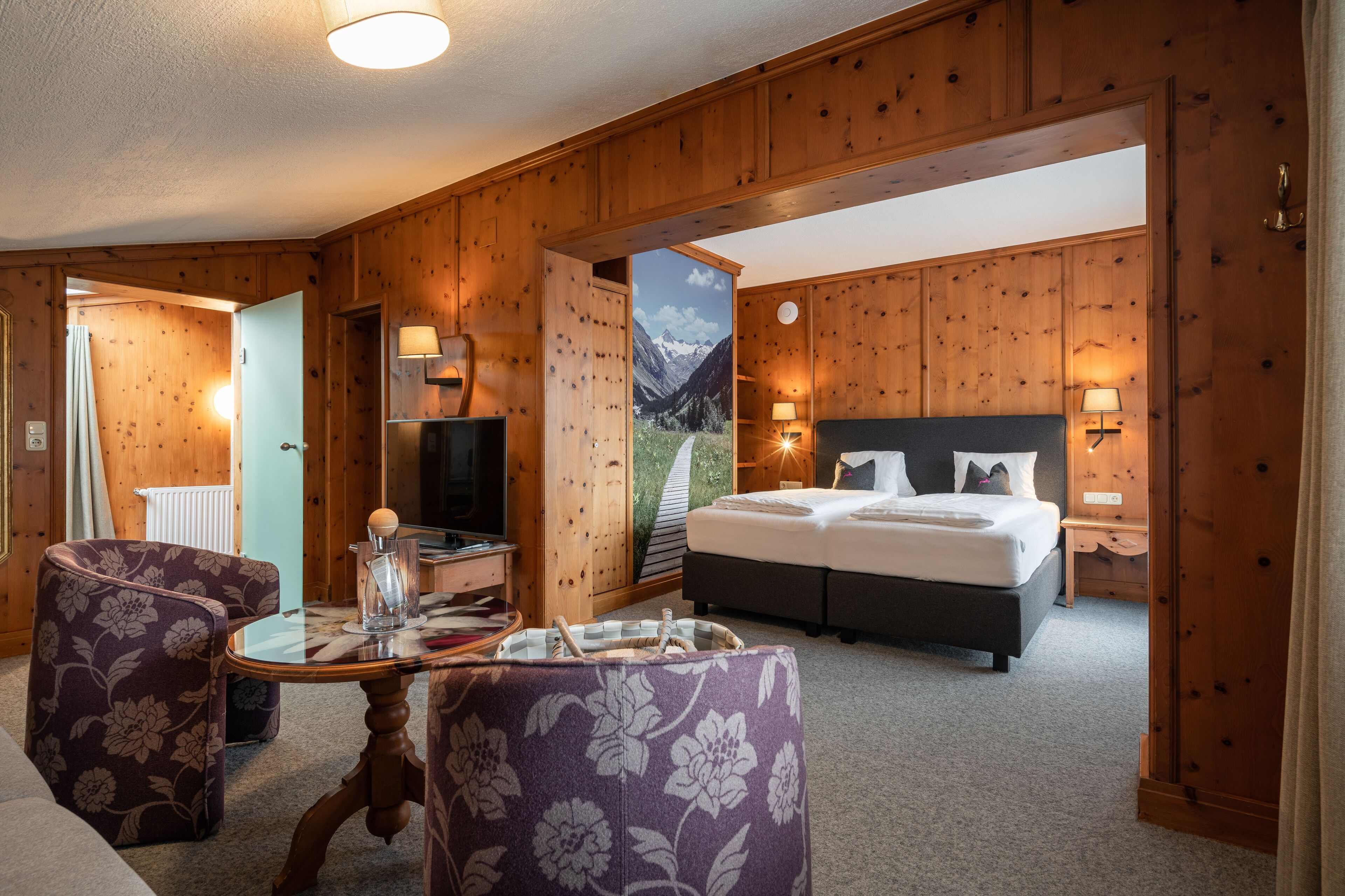 Ein Zimmer mit Holzwänden, einem Bett, einem Tisch und zwei Stühlen.