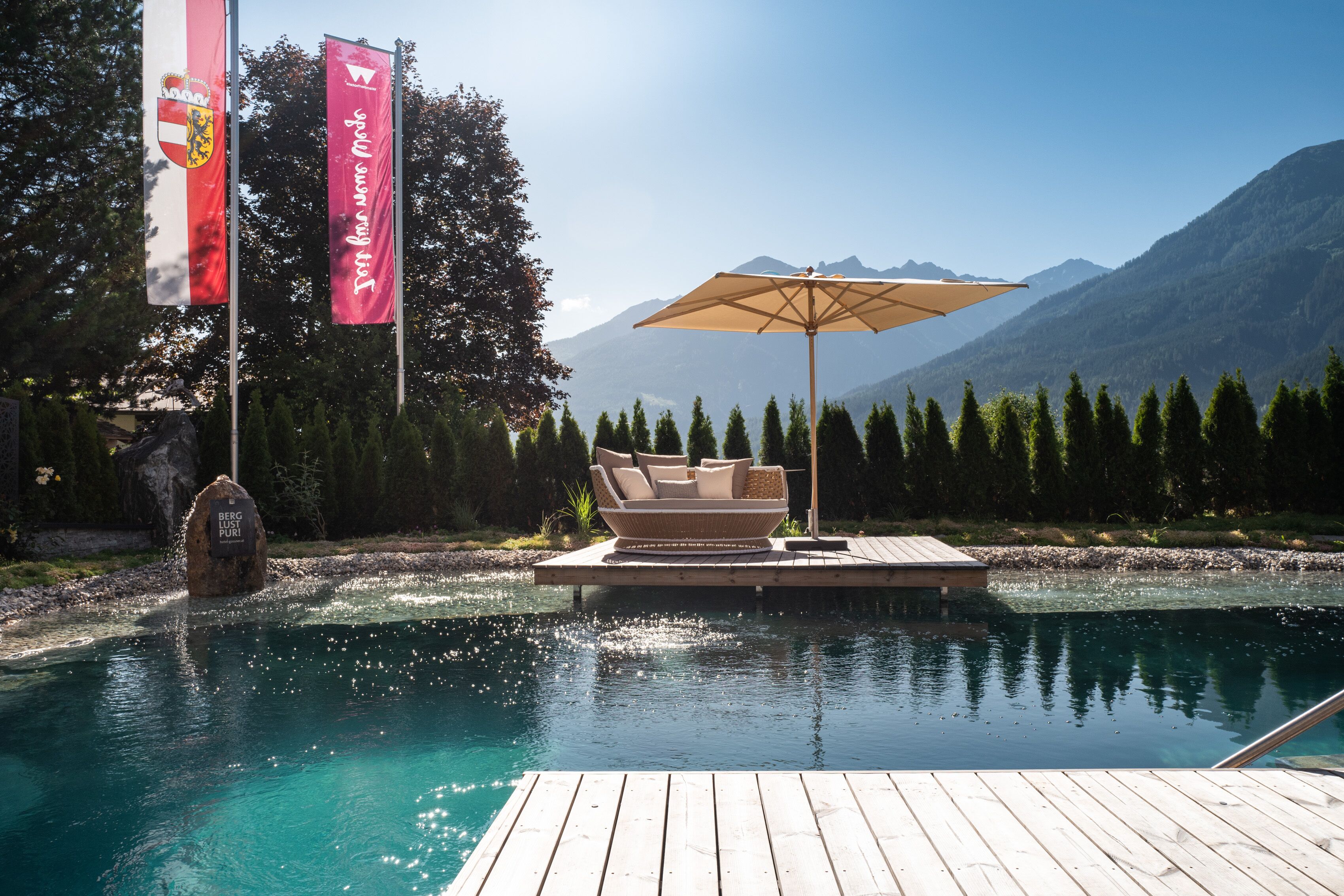 A pool with a wooden deck, a lounge chair, and an umbrella.