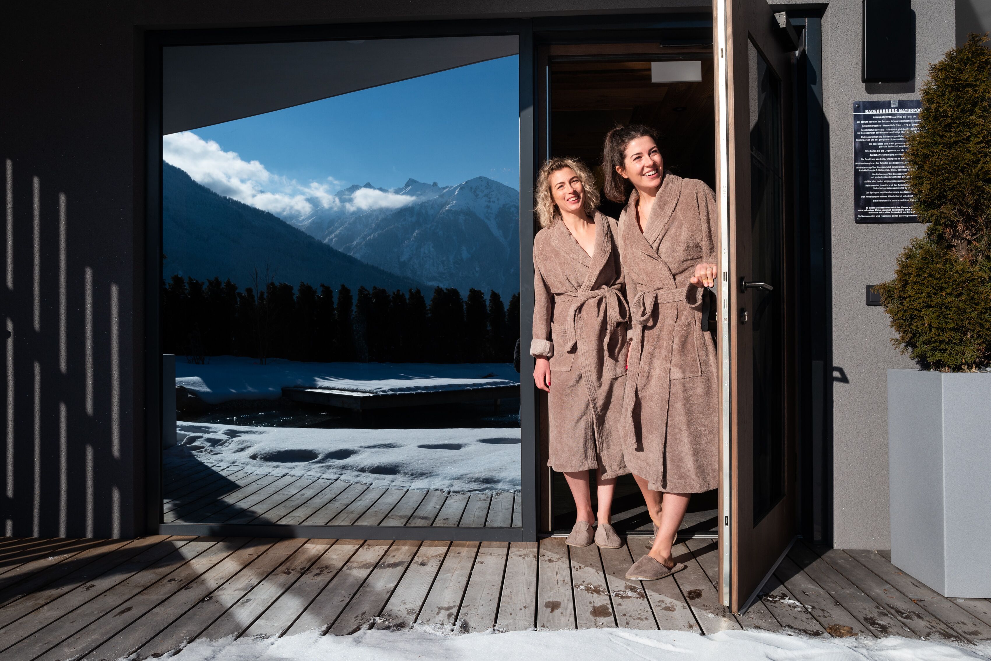 A wooden deck with snow, a large glass door with a mountain view, and a sign on the wall.
