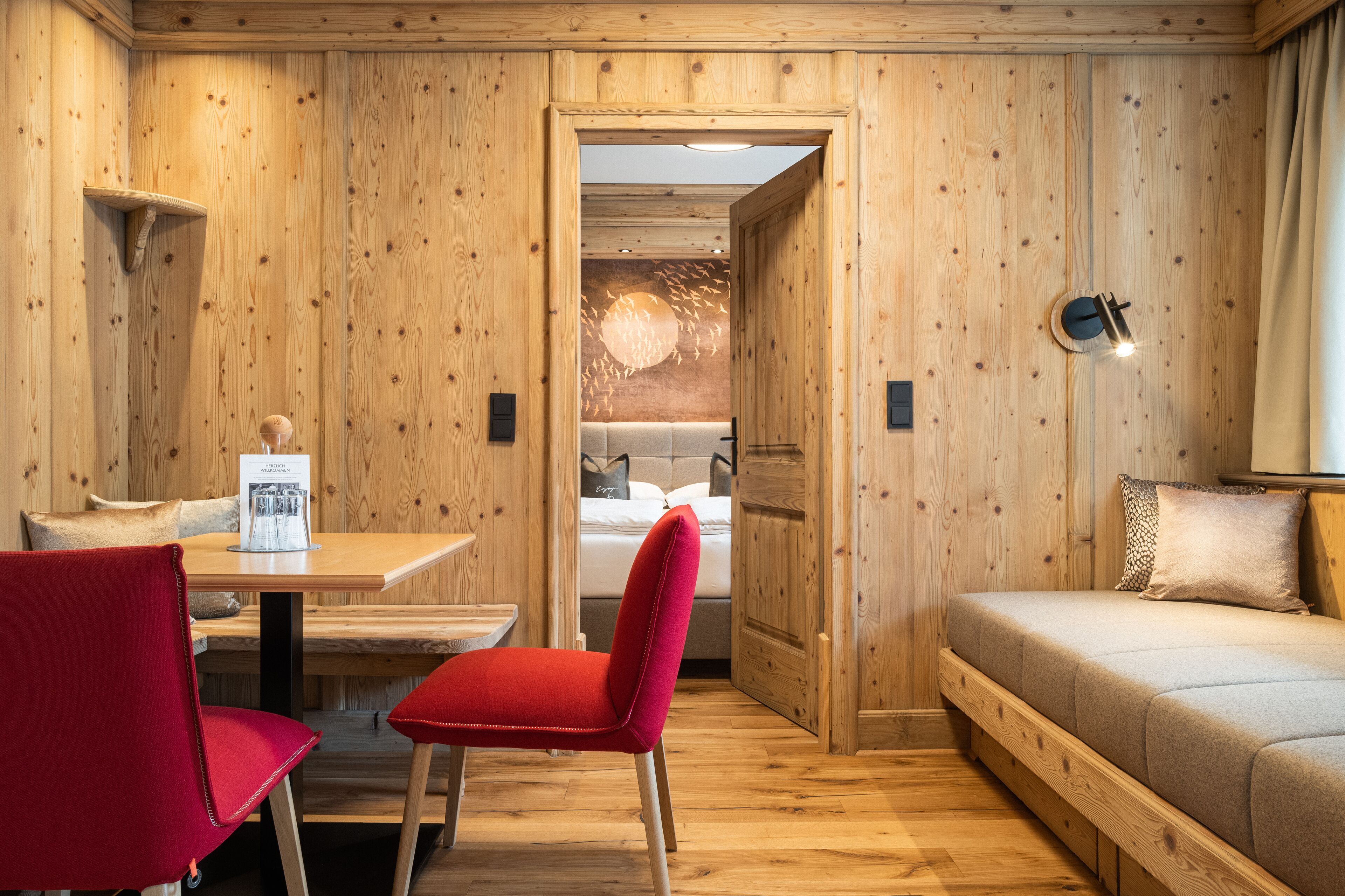 A wooden-paneled room with a bed, a table with chairs, and a wall-mounted light fixture.