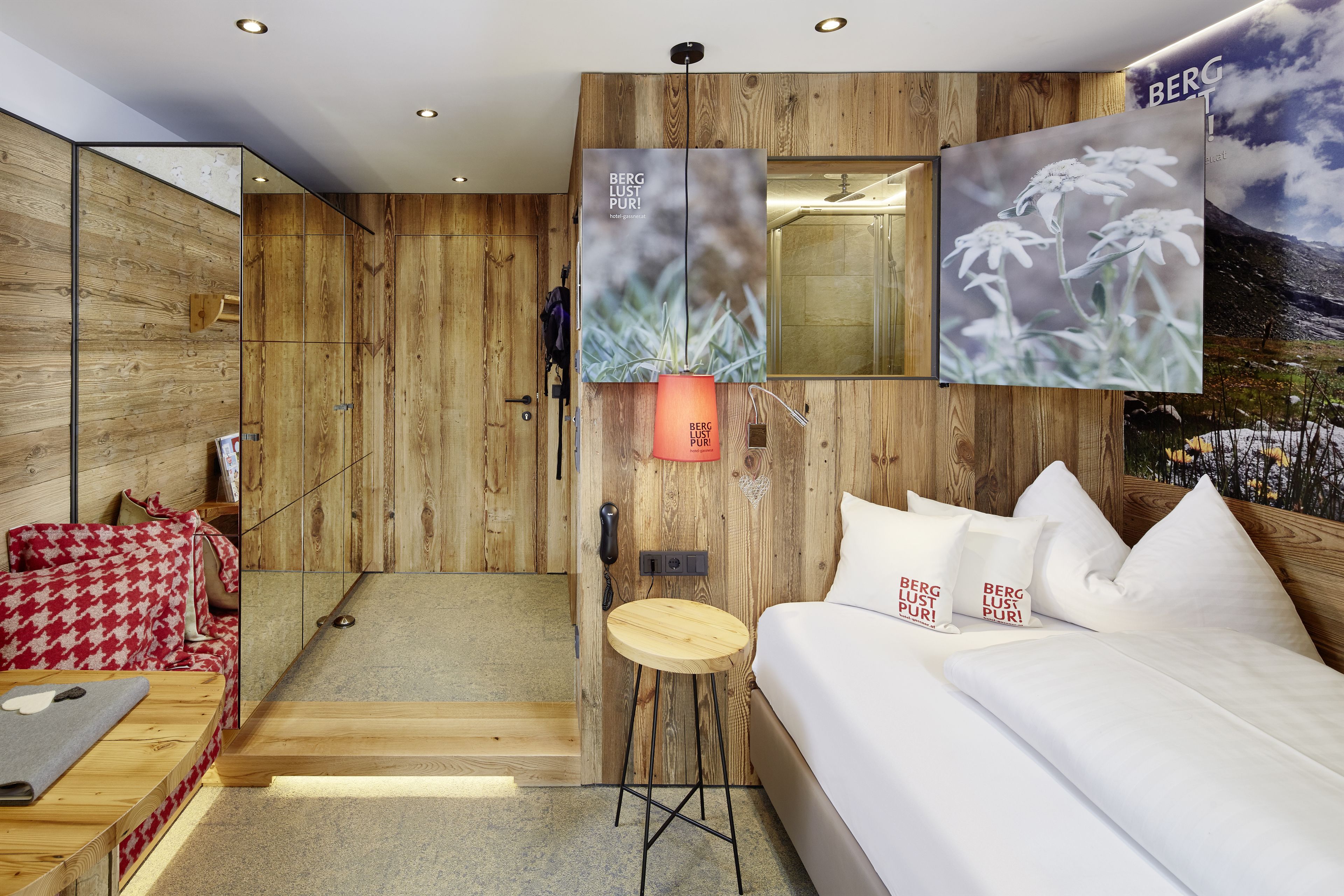 A modern hotel room with wooden panel walls, a bed with white bedding, a small wooden stool, and a mounted artwork of flowers.