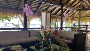 An outdoor seating area with a thatched roof, a sofa, and a table with a vase of flowers. - Pension Raita (Ahe)
