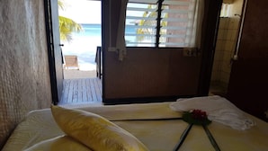 A hotel room with a bed, a window with a view of the beach, and a towel on the bed. - Pension Raita (Ahe)