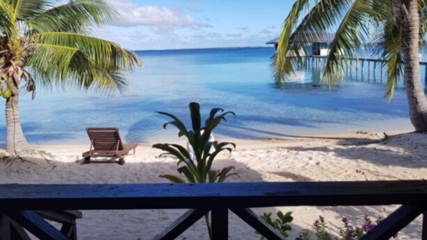 A beach view with a wooden deck, a lounge chair, and palm trees. - Pension Raita (Ahe)