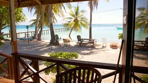 A beach view from a covered area with wooden furniture and palm trees. - Pension Raita (Ahe)