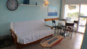 Une pièce avec un canapé blanc, une petite table sur laquelle est posé un panneau indiquant «Australie», une horloge et une fenêtre donnant sur la mer.