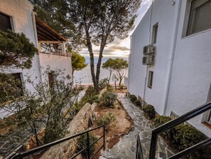 A coastal building with a stone pathway leading to a terrace overlooking the sea. - Agi Marina 6 Apartamento for rent in Roses Girona. (Roses)