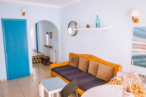 A cozy room with a blue door, a wooden sofa with cushions, a small table, and a wall clock. - Agi Marina 6 Apartamento for rent in Roses Girona. (Roses)