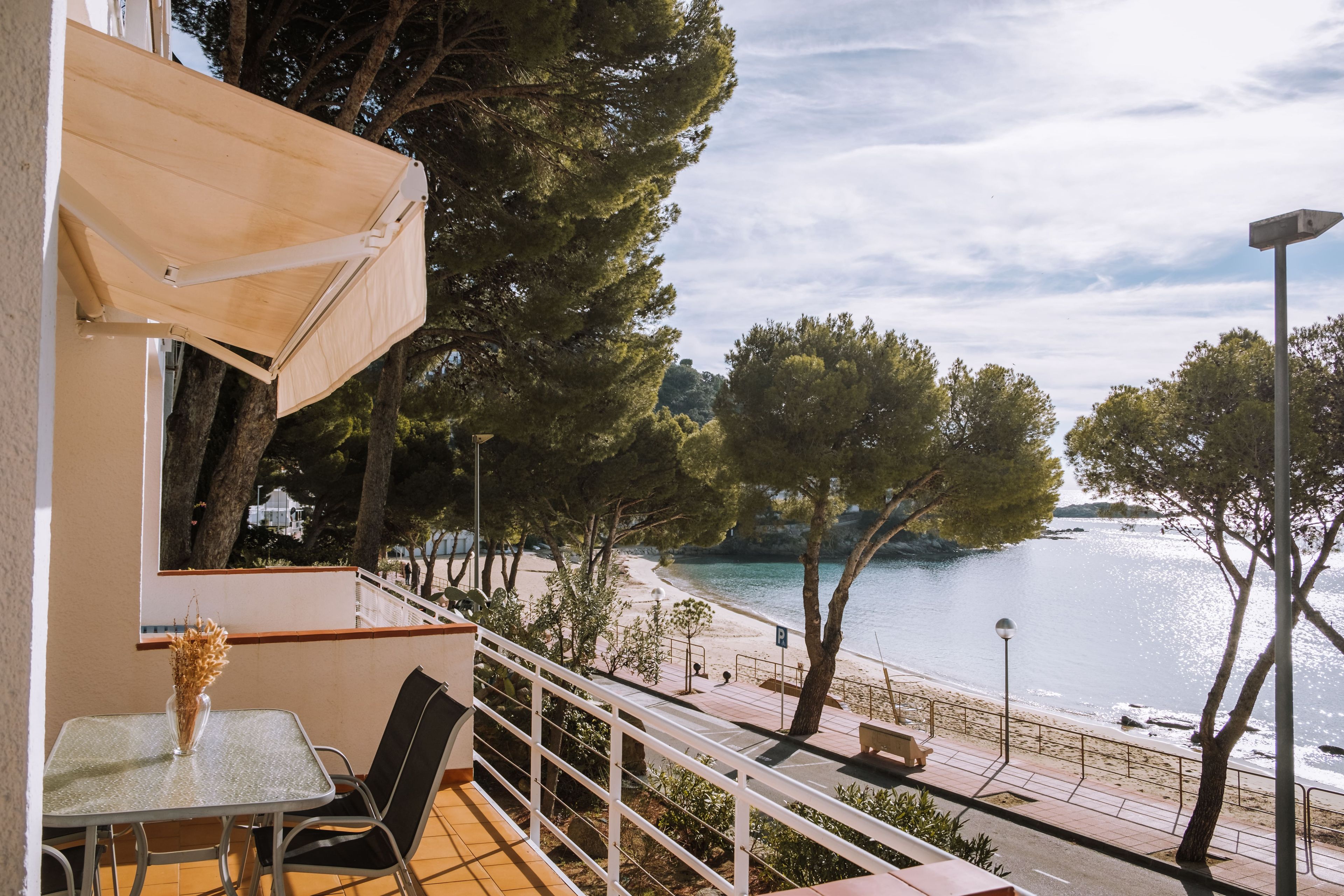 A balcony with a table and chairs, overlooking a beach and water.