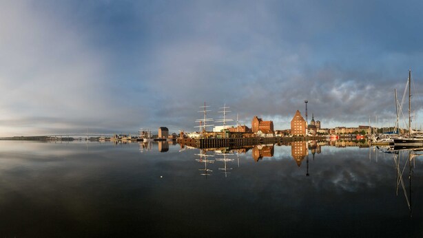 Ein Hafen mit ruhiger Wasseroberfläche, die Gebäude und Boote spiegelt.