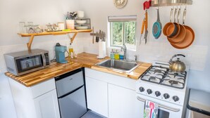 Une cuisine compacte équipée d’un four à micro-ondes, d’une machine à café, d’un évier, d’une cuisinière et de quelques ustensiles de cuisine suspendus.