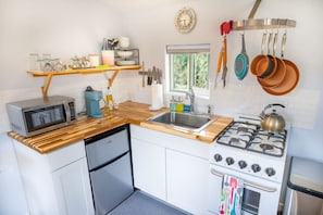 A compact kitchen with a microwave, coffee maker, sink, stove, and hanging pots.