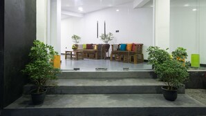 Un área de recepción con un banco y sillas de madera, una mesita y plantas en macetas.